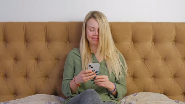 Woman browsing social media news feed and internet on new smart phone in bedroom