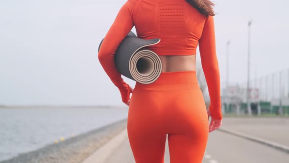 A woman carries a yoga mat in her hands after an outdoor workout. The girl carries a fitness mat. Ba