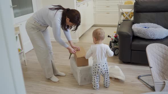 Mother with Baby Unpacking Unboxing Cardboard Package Box at Home Woman Received a Delivered Package