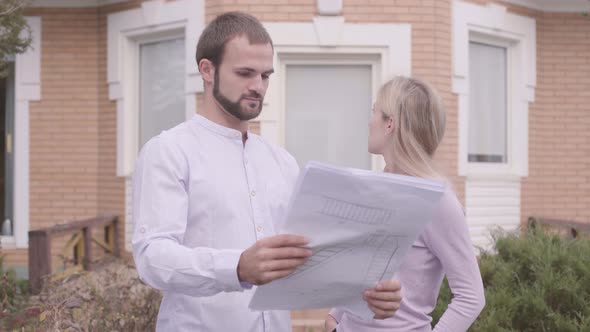 Professional Caucasian Male Archtect Showing Blueprints and Newly Built House To the Customer