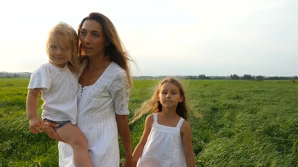 Happy Family Mother and Her Little Daughters Walk on the Green Grass