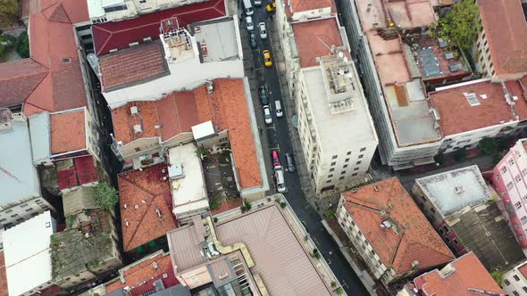 Aerial top down view of cars driving down a narrow alley street surrounded by tall European resident