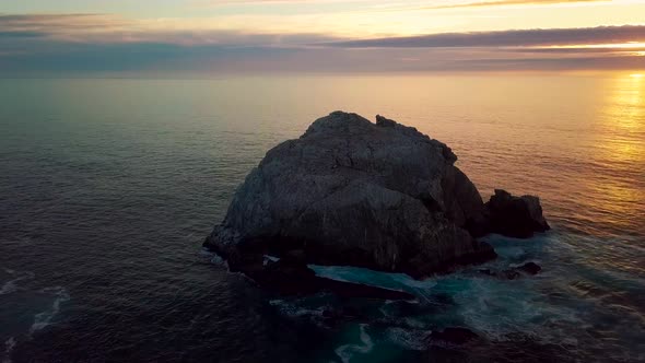 Slow sunset orbit around huge ocean rock and crashing waves at Sand Dollar Beach in Big Sur Californ