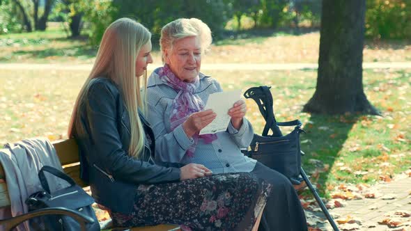 Middle Close Up of Old Woman Reading a Letter To Pretty Young Woman in Park