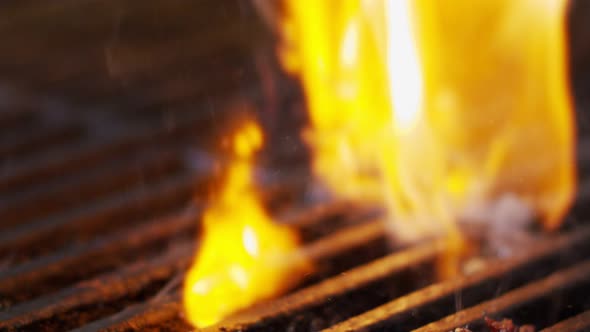 Slow motion of beef hamburger on a grill in close up with flames and smoke