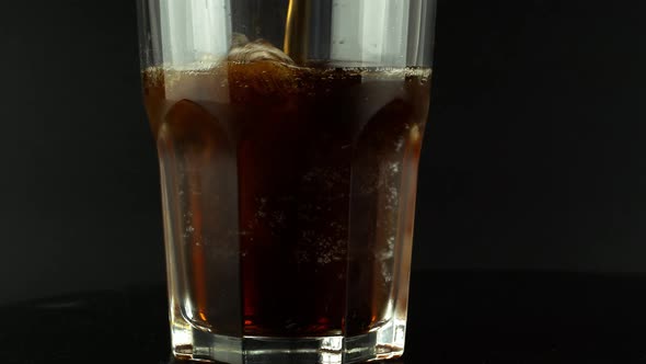 Pouring cola with ice cubes close-up. Cola with Ice and bubbles in glass on a black background.