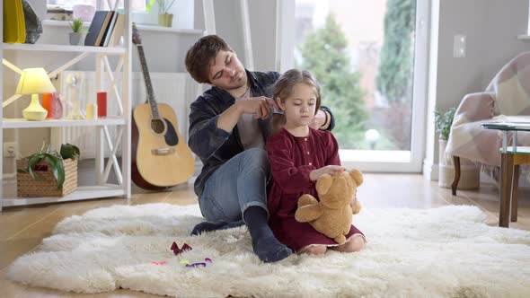 Wide Shot of Happy Pretty Girl Playing with Teddy Bear As Loving Father Combing Long Curly Hair of