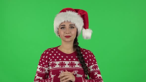 Portrait of Sweety Girl in Santa Claus Hat Is Looking with Tenderness with Folded Arms in Front 