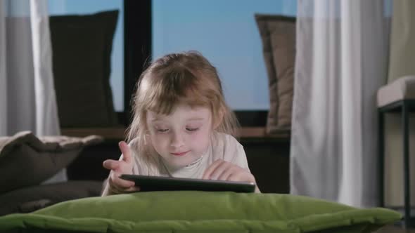 Preschooler Girl Playing Games Using Digital Tablet Lying On Sofa Alone.