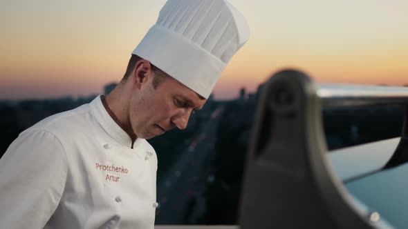 Portrait of a professional chef: he looks into the camera while having a barbecue on the roof
