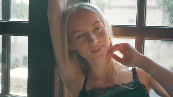 fashion portrait of a beautiful young woman with blue eyes and blonde hair poses near the window
