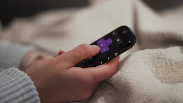 Close up of remote control, woman changing channels on Roku device TV