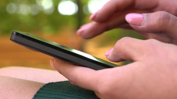 A Young Asian Woman Works on A Smartphone in A Park on A Sunny Day