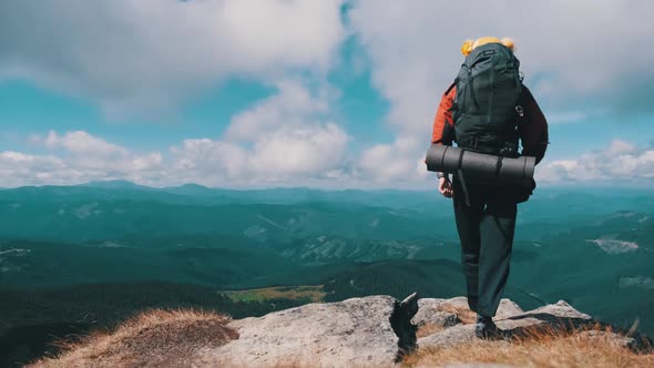 Tourist with Backpack on the Top of Mountain Near the Cliff Raises Hands To Side