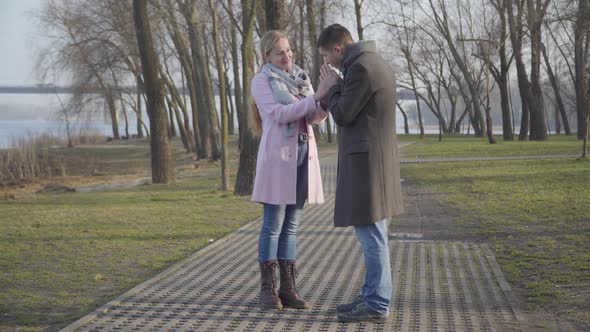 Wide Shot, Young Elegant Caucasian Man Warming Hands of Older Woman in City Park. Happy Couple with