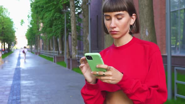 Pretty Millenial Girl in Red Top Chatting in Her Phone on the Modern Street