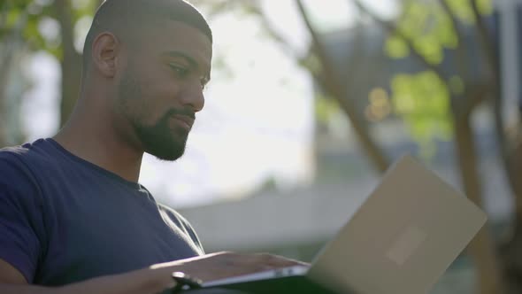 Bottom View of Young Afro-American Man in Park Working on Laptop