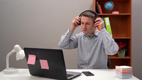 A Young Worker Communicates with a Client at an Online Conference From the Office Through Headphones