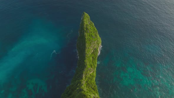 Lush green Sekartaji cliff surrounded by turquoise and blue sea water, aerial