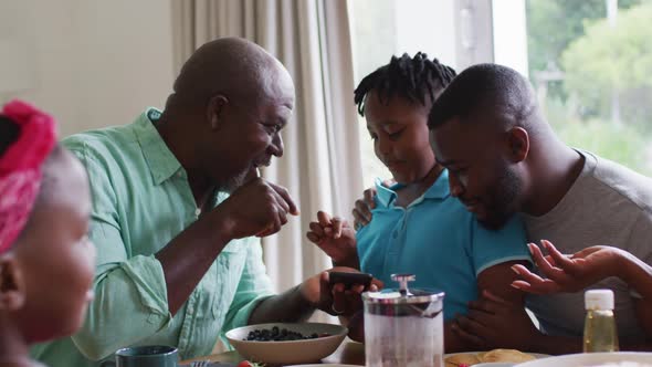 African american grandfather, father and son smiling while using smartphone together at home