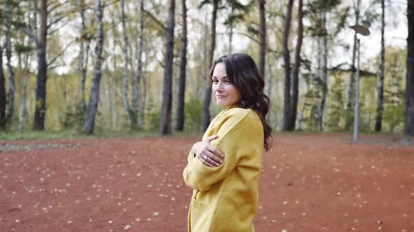 A Young Woman in a Yellow Sweater Walks in the Autumn Park. Brunette Woman Basks in the Cold Forest