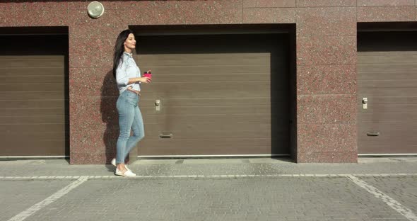 Confident Lady Walking with Cup of Beverage in Hand and Poses Outdoors