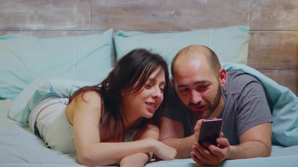 Wife in Pajamas Laughing While Her Husband Is Showing Something on Phone