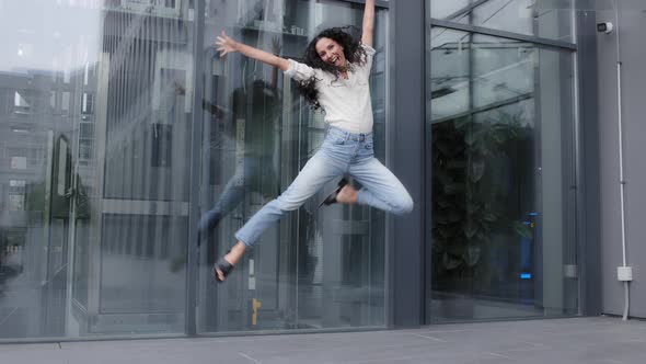 Woman with Long Curly Hair Dynamic Jumping Into Air Laughing Smiling Celebrating Victory Winning