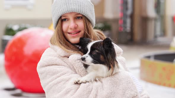 Beautiful Girl with Dog Papillon in Her Arms on Winter Christmas Streets