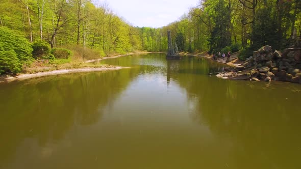 Drone fast footage of a lake in a forest park,  a beautifully designed concrete, curb foot bridge co