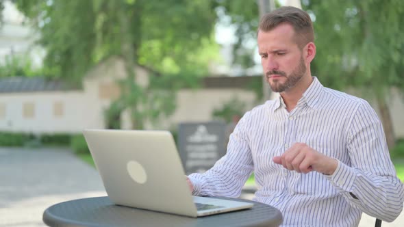 Middle Aged Man with Laptop Having Wrist Pain in Outdoor Cafe