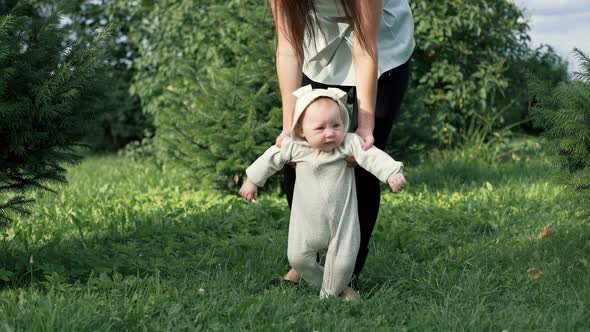 Cute Funny Happy Baby Making First Steps on a Green Lawn in a Sunny Summer Garden