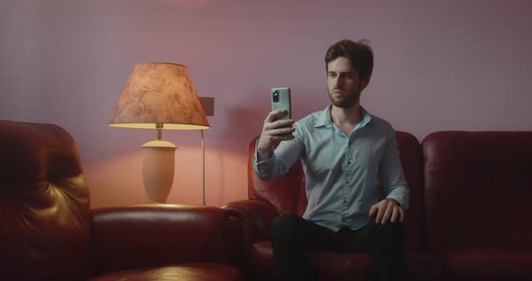 Guy takes selfies with smartphone at home on the red sofa