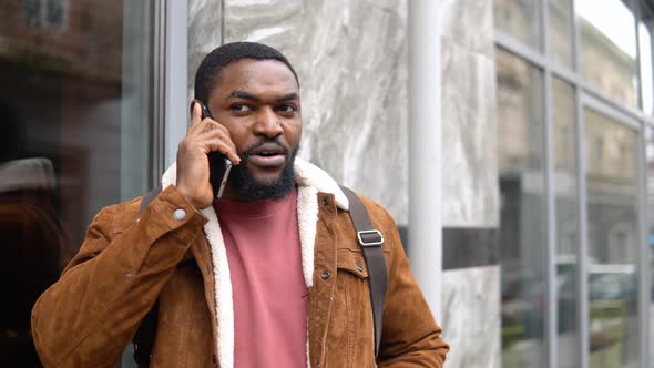 Black Man with Shoulder Backpack Stands Outdoor Near the Office Center