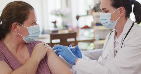 Caucasian woman and female doctor wearing face masks, vaccinating