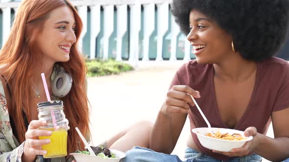 Female friends sitting on ground eating lunch