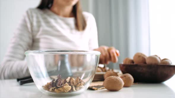 Young Woman Is Cracking a Walnuts and Collecting It in Glass Bowl, Close-up