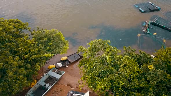 Drone view of boats and fishing equipment sitting on the shore of a lake on a fishing farm in the To