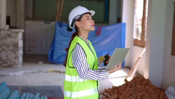 Asian engineer or Young woman Architect put on a helmet for safety and user laptop for check Bluepri