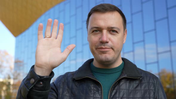 Millennial Guy Looking at Camera Smiling and Waving Hello Greeting Gesture Standing at City Street