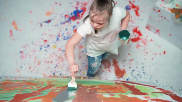Girl with Down Syndrome Draws with a Brush on a Large Canvas in a White Room Girl with Special Needs