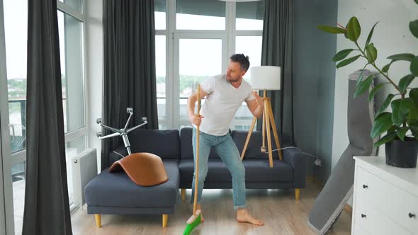 Man Cleaning the House and Having Fun Dancing and Singing with a Broom