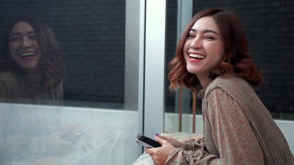 slow-motion of cheerful young woman holding smartphone at window