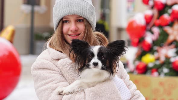 Beautiful Girl with Dog Papillon in Her Arms on Winter Christmas Streets