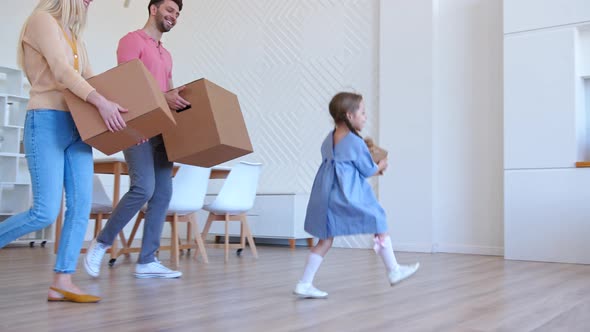 Funny little preschooler girl helps parents carry cardboard boxes