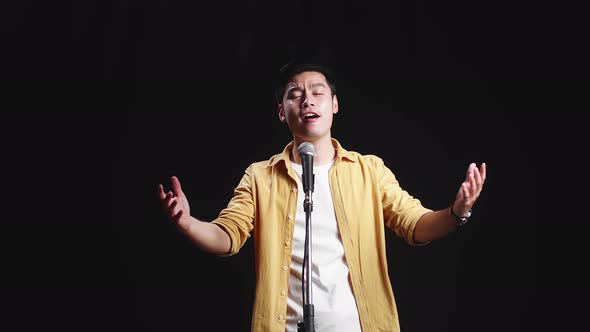 Asian Man Singer Singing Into Microphone On Black Background