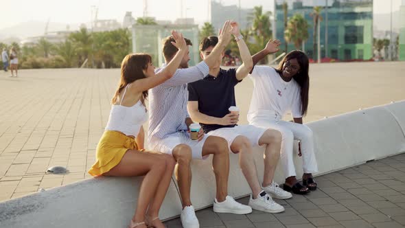 Multiracial Happy Friends Giving High Five and Smiling with Takeaway Coffee in Hands on Summer Day