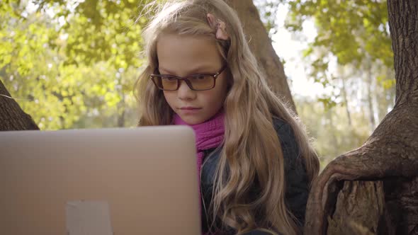 Close-up Portrait of a Young Caucasian Teenage Girl in Photochromic Glasses Sitting with Laptop