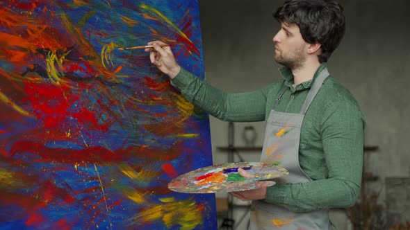 Inspired Male Artist Puts the Finishing Touches to His Painting in a Bright Studio