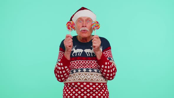 Grandfather in Christmas Sweater Holding Candy Striped Lollipops Hiding Behind Them Fooling Around